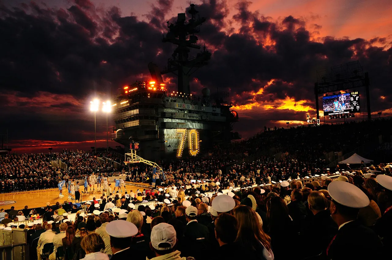 The sun sets over the crowd at a college game played on an aircraft carrier deck