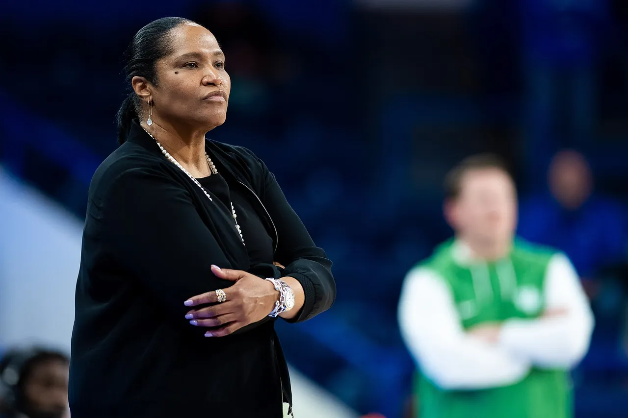 A women's basketball head coach watches from the sideline during a tournament game