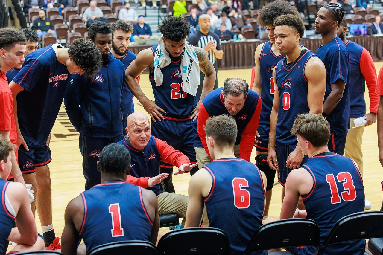 A Division I men's basketball team huddles around its head coach during a game timeout.