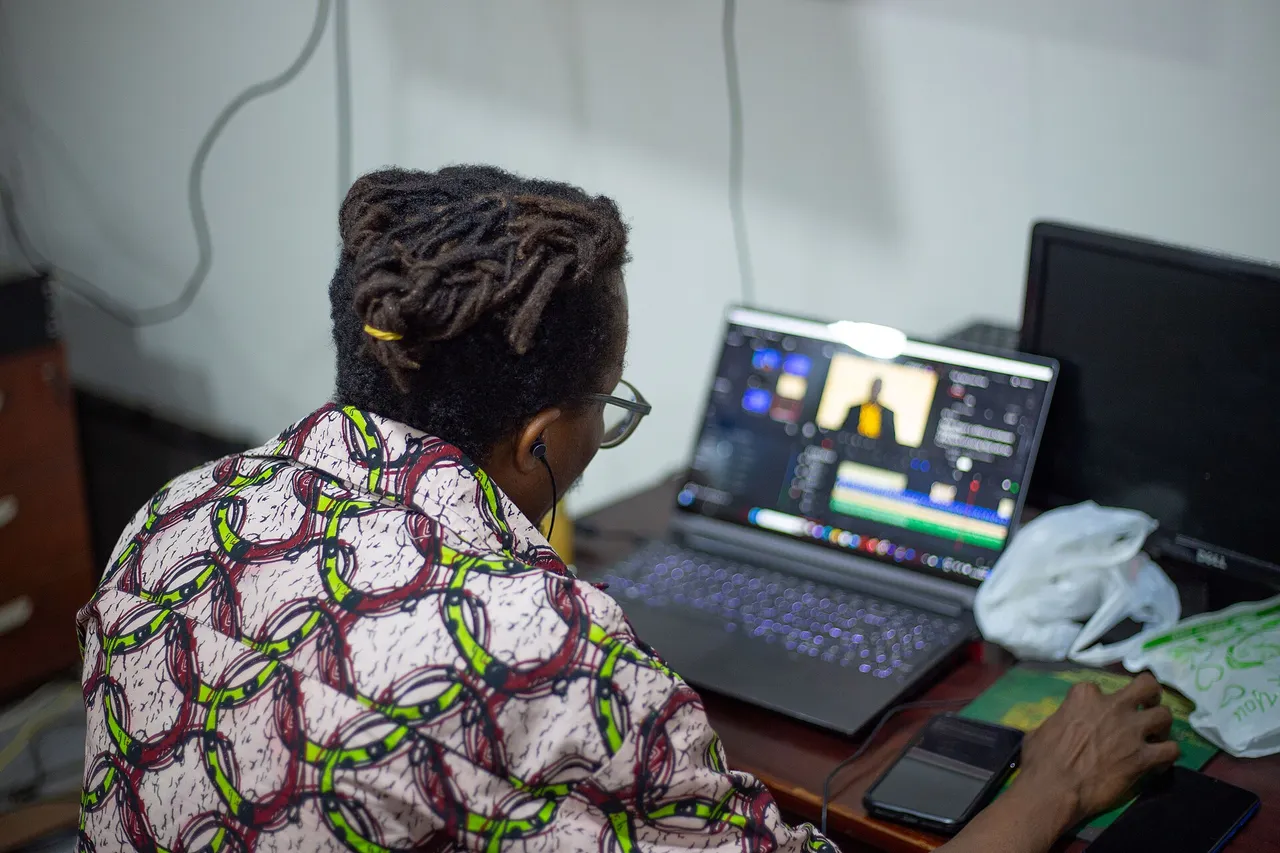 A person seen from behind edits video on a laptop at a desk.