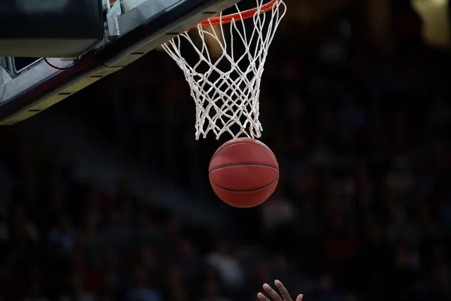 A basketball dropping through a white net under arena lights