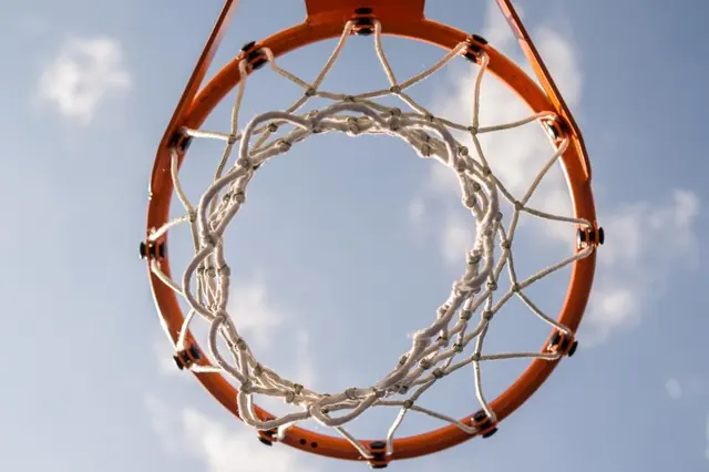 Looking straight up through an orange rim and net at the sky