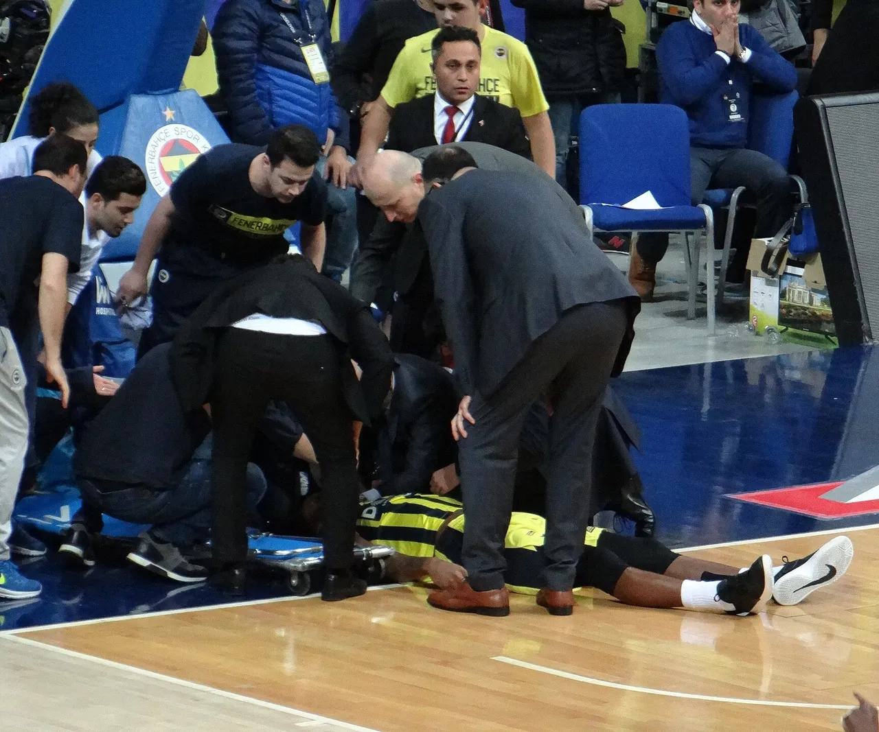 A professional basketball player lies on the court while medical staff and officials gather around him.