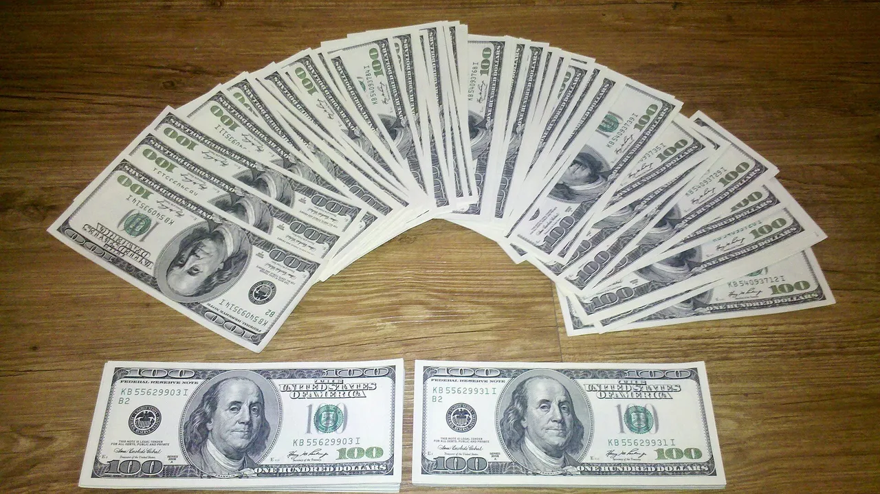A fan of US one-hundred-dollar bills spread on a wooden table.