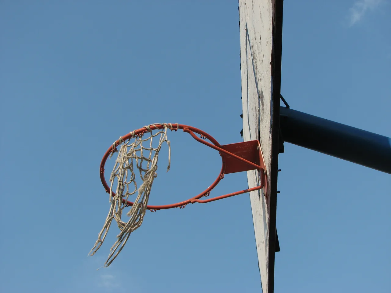 A frayed net on a weathered outdoor hoop against the sky