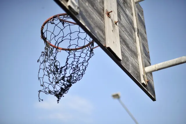 A worn net hanging from a wooden backboard