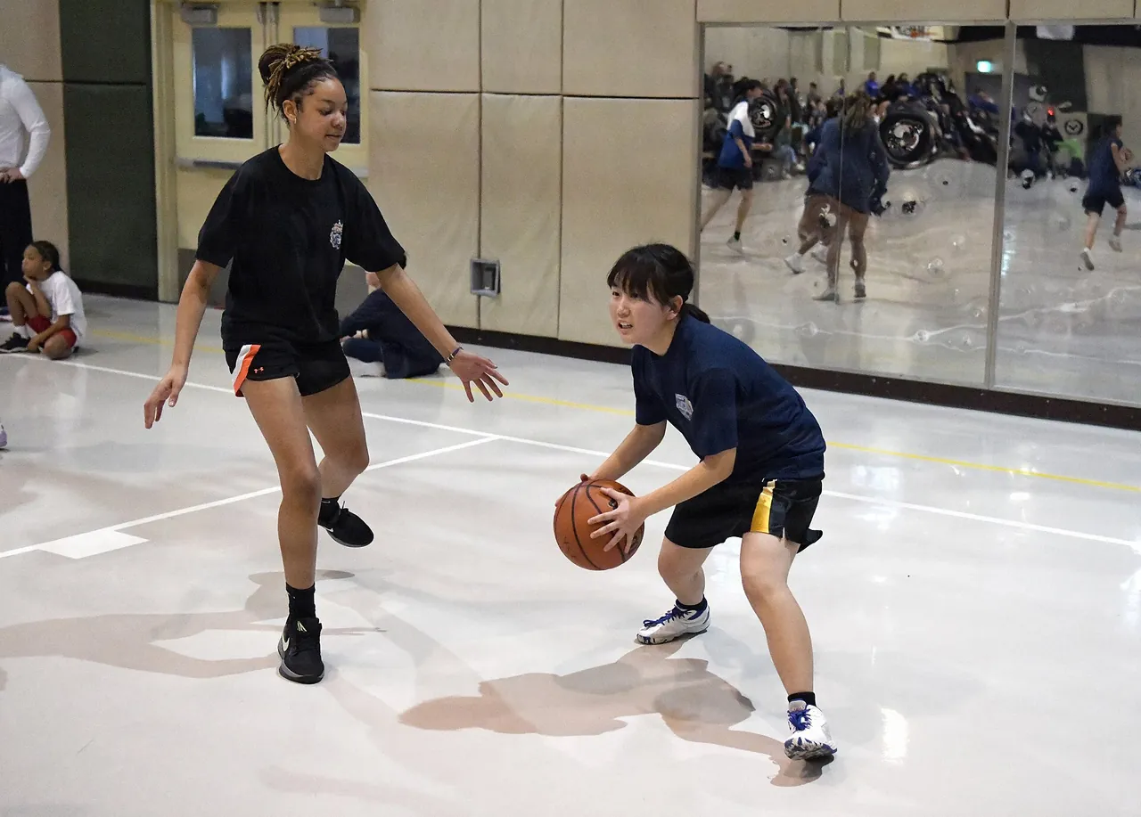 A coach teaches ball handling one on one to a young player in a gym